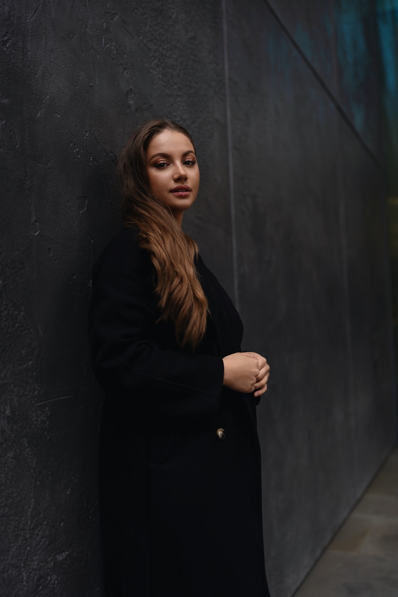 A woman leaning against a wall in a black coat